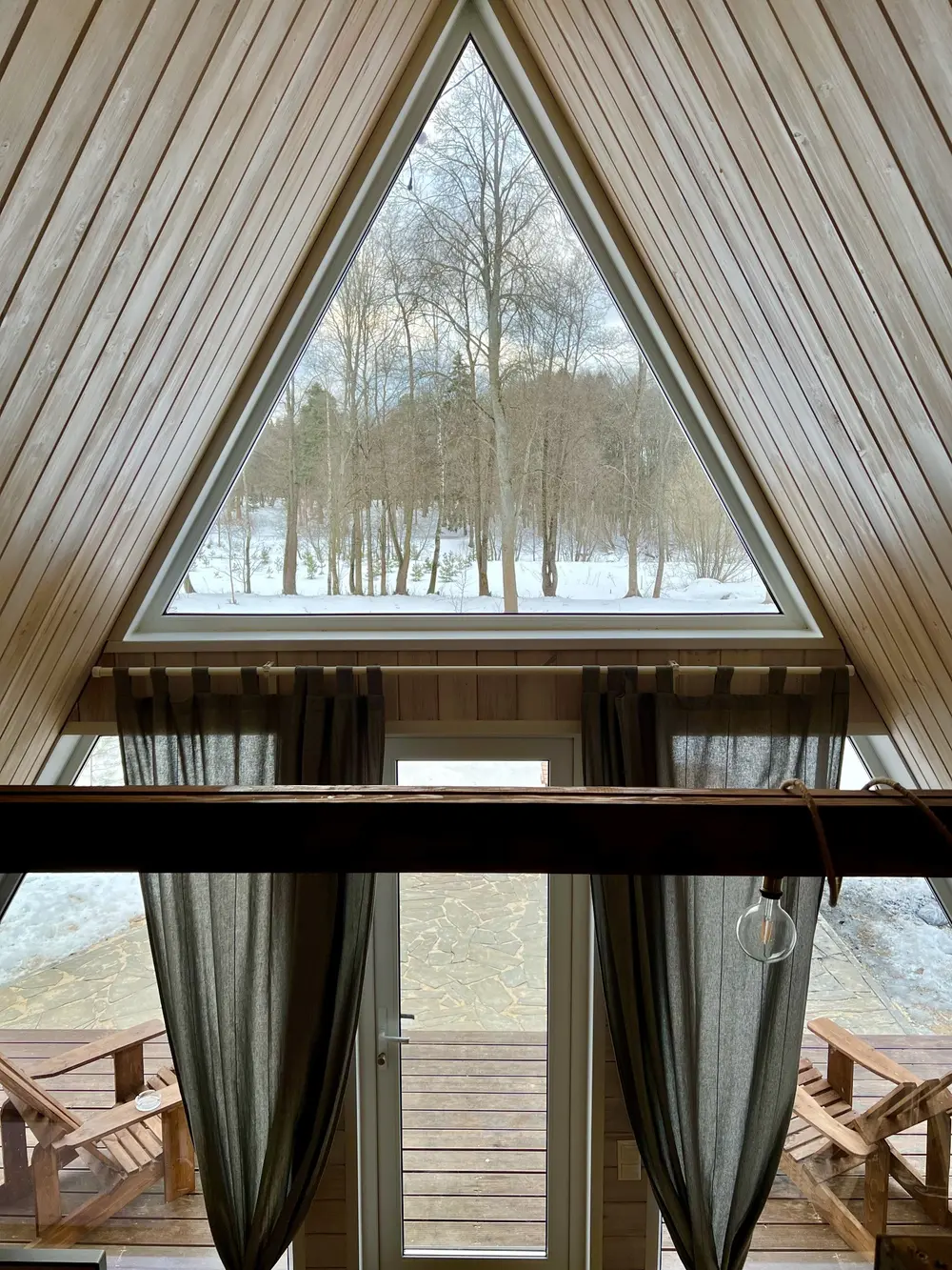 Вид с верхнего уровня A-frame дома Indie House на панорамное окно и лес